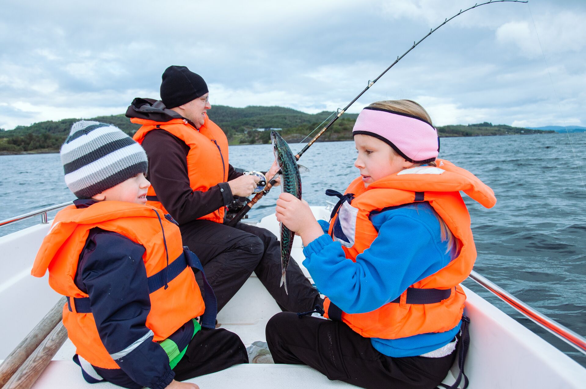 Two kids and a man wearing lifejackets on a fishing boat. 